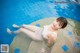 A woman in a white bathing suit laying on the edge of a pool.