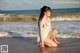 A woman in a white dress crouching on the beach.