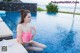 A woman in a pink bikini sitting by a swimming pool.