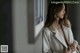 A woman in a white coat leaning against a wall.