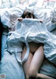 A naked woman laying in bed under a blanket.